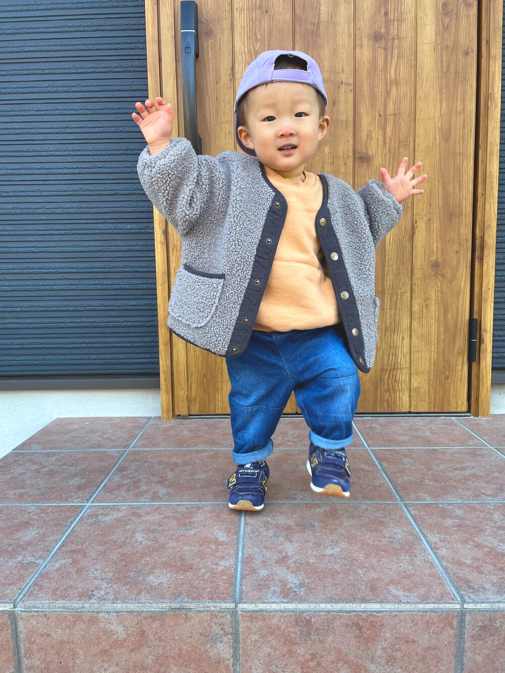 オレンジ系のスウェット、グレー系のノーカラージャケット、ブルー系のデニムパンツを着用したキッズの冬コーディネートの3枚目の写真