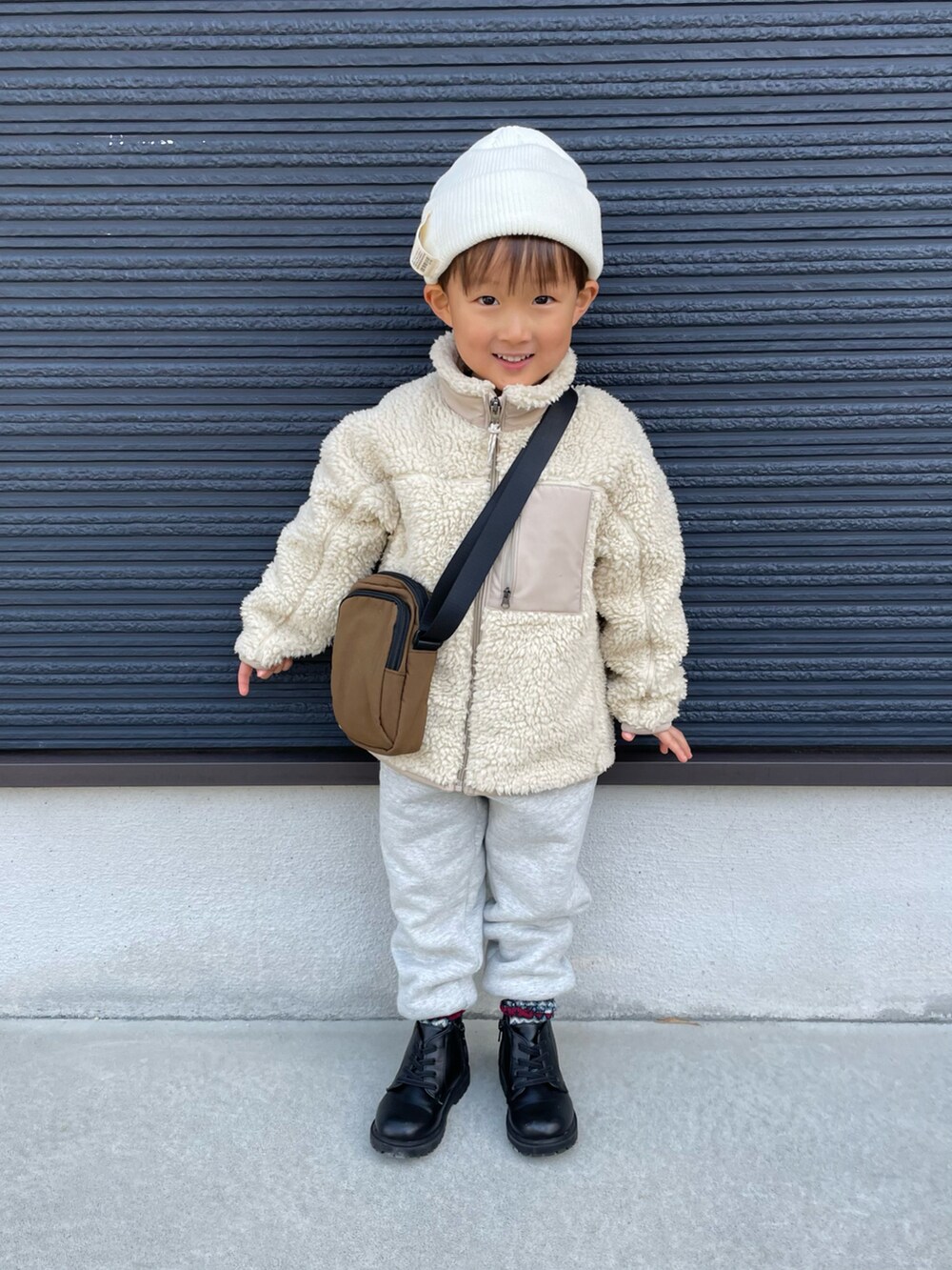 ブラウン系のショルダーバッグ、ベージュ系のその他アウター、グレー系のスウェットパンツを着用したキッズの冬コーディネートの3枚目の写真