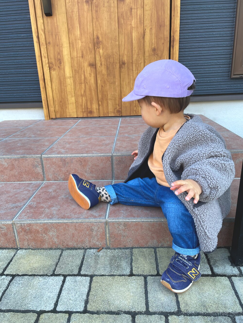 オレンジ系のスウェット、グレー系のノーカラージャケット、ブルー系のデニムパンツを着用したキッズの冬コーディネートの2枚目の写真