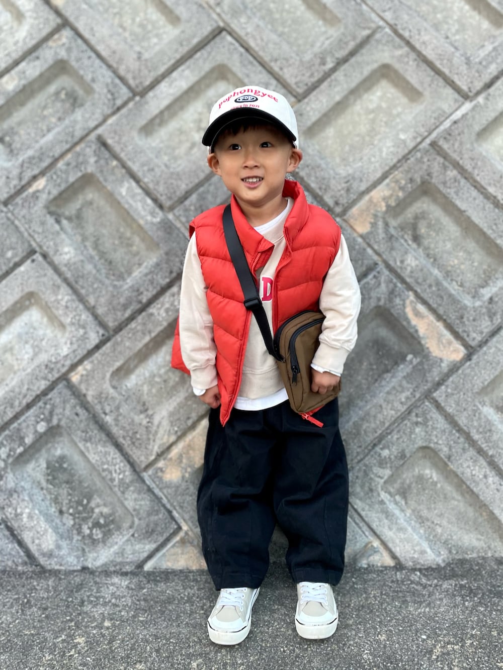 オレンジ系のダウンベスト、ベージュ系のスウェット、ブラウン系のショルダーバッグを着用したキッズの秋コーディネートの4枚目の写真