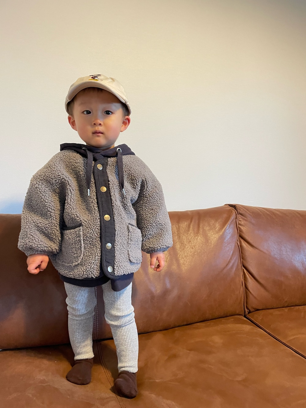 パープル系のパーカー、グレー系のノーカラージャケット、ベージュ系のキャップを着用したキッズの冬コーディネートの2枚目の写真