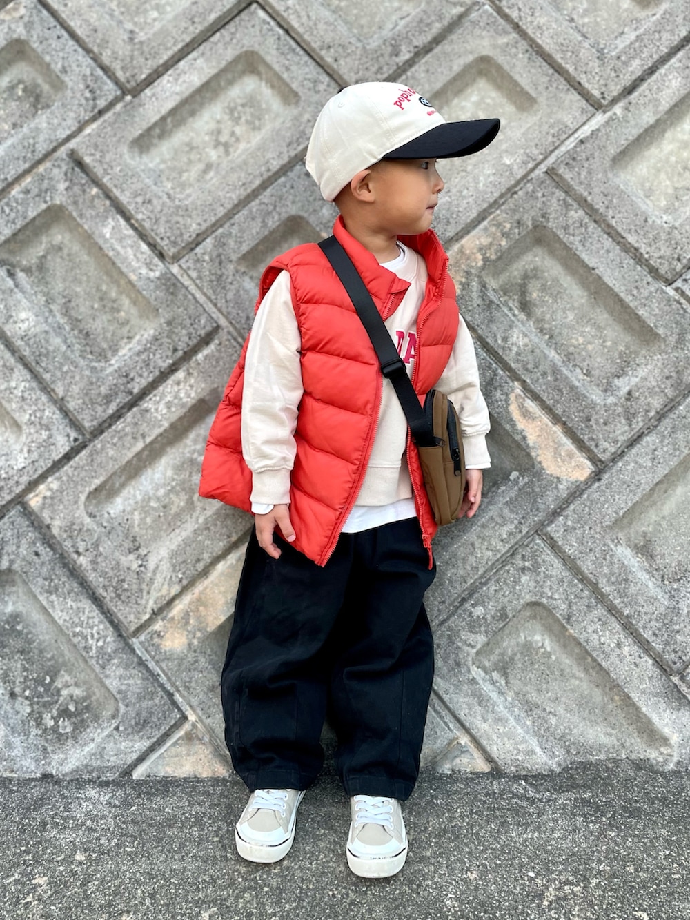 オレンジ系のダウンベスト、ベージュ系のスウェット、ブラウン系のショルダーバッグを着用したキッズの秋コーディネートの2枚目の写真