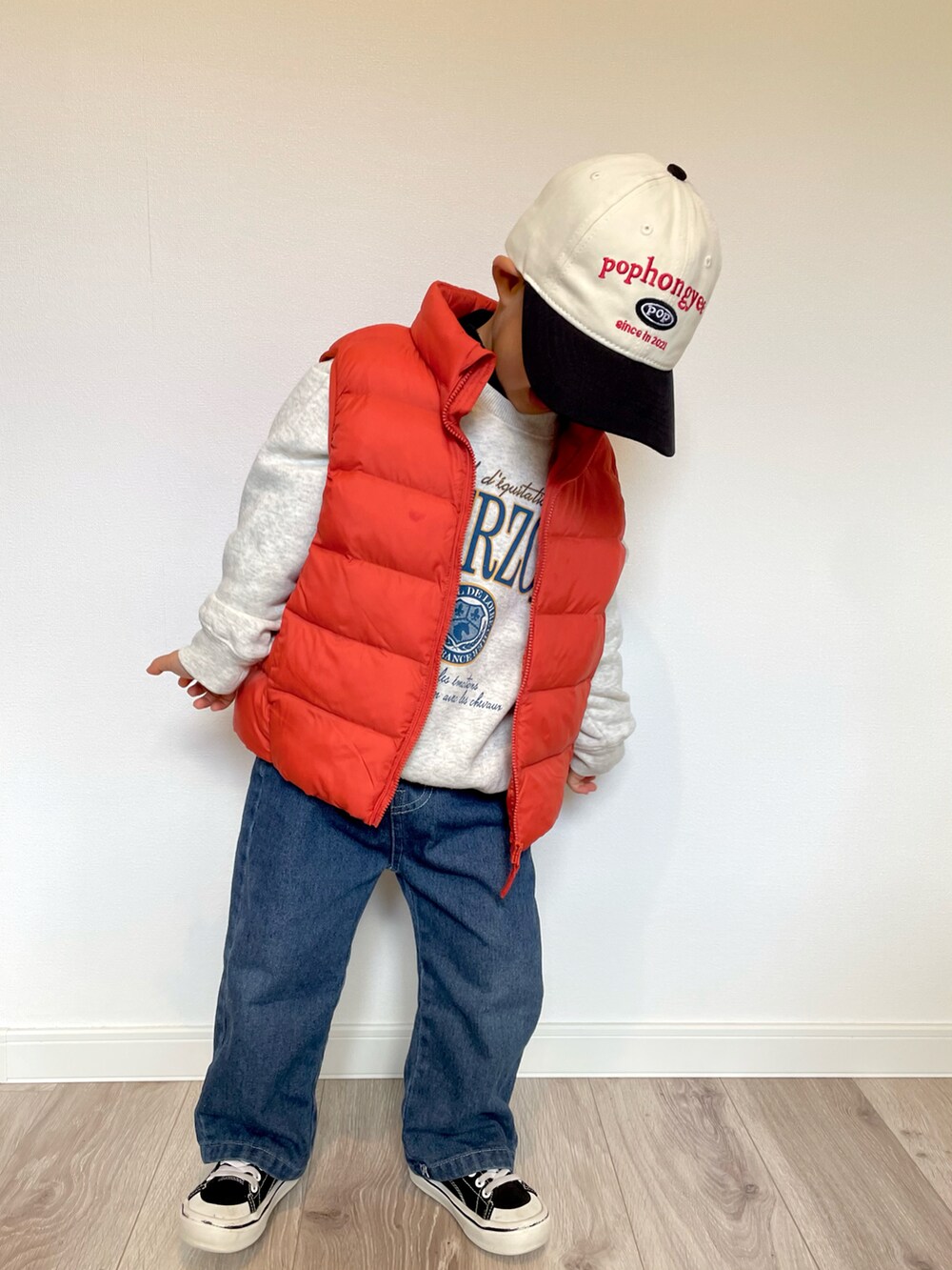 オレンジ系のダウンベスト、グレー系のスウェット、ブルー系のデニムパンツを着用したキッズの冬コーディネートの2枚目の写真