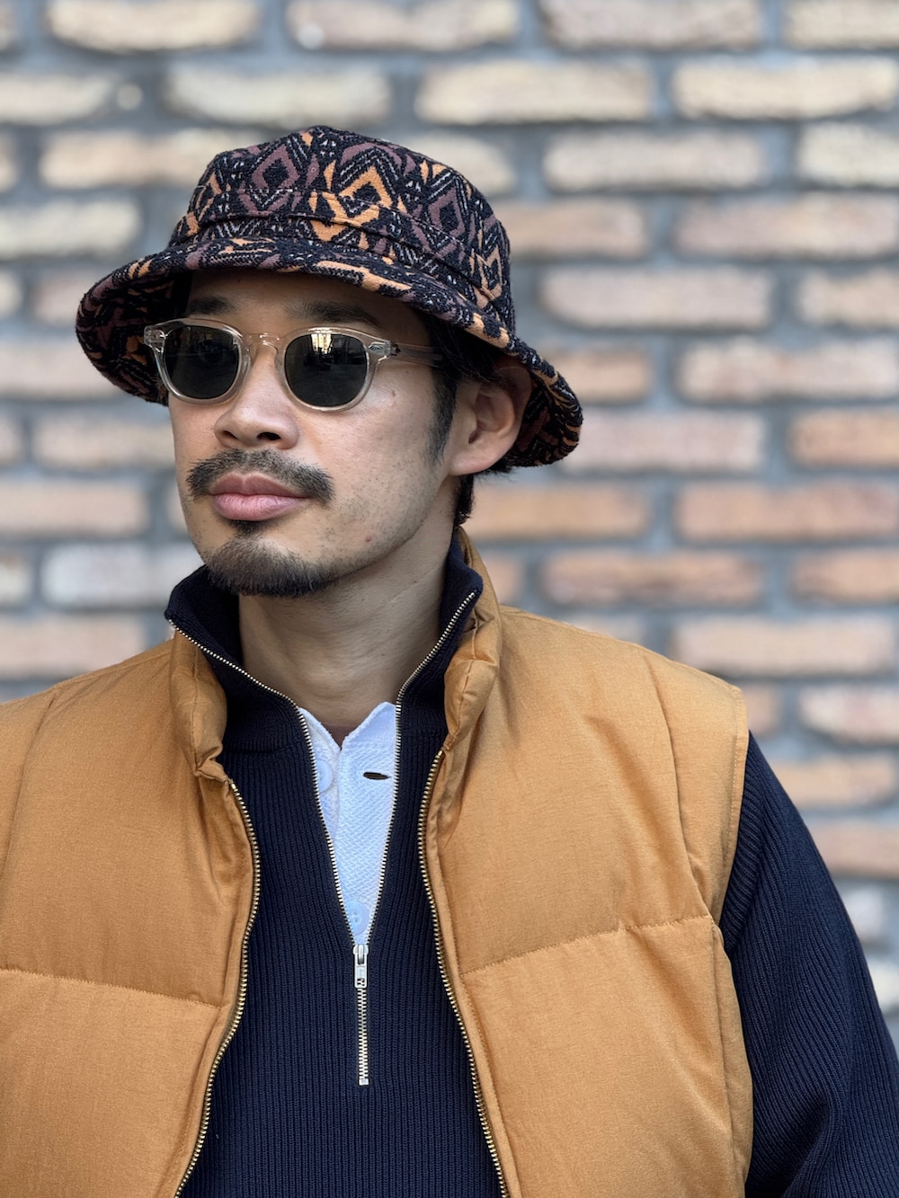 ゴールド系のダウンベスト、ブラウン系のトートバッグ、その他のハットを着用したメンズの冬コーディネートの3枚目の写真