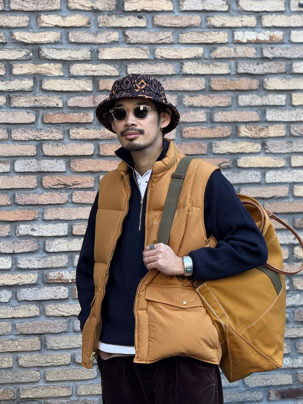 ゴールド系のダウンベスト、ブラウン系のトートバッグ、その他のハットを着用したメンズの冬コーディネートの2枚目の写真