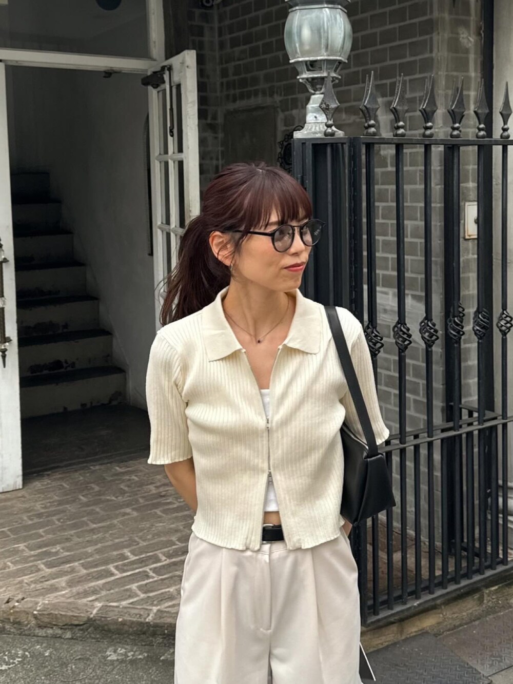 ホワイト系のニット/セーター、ホワイト系のスラックス、ブラック系のショルダーバッグを着用したレディースの夏コーディネートの3枚目の写真