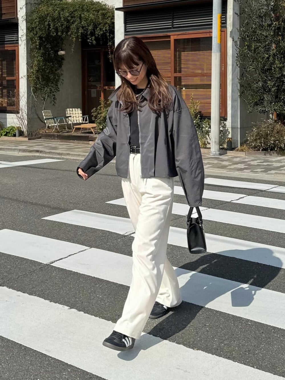 グレー系のブルゾン、ブラック系のTシャツ/カットソー、ホワイト系のスラックスを着用したレディースの春コーディネートの2枚目の写真