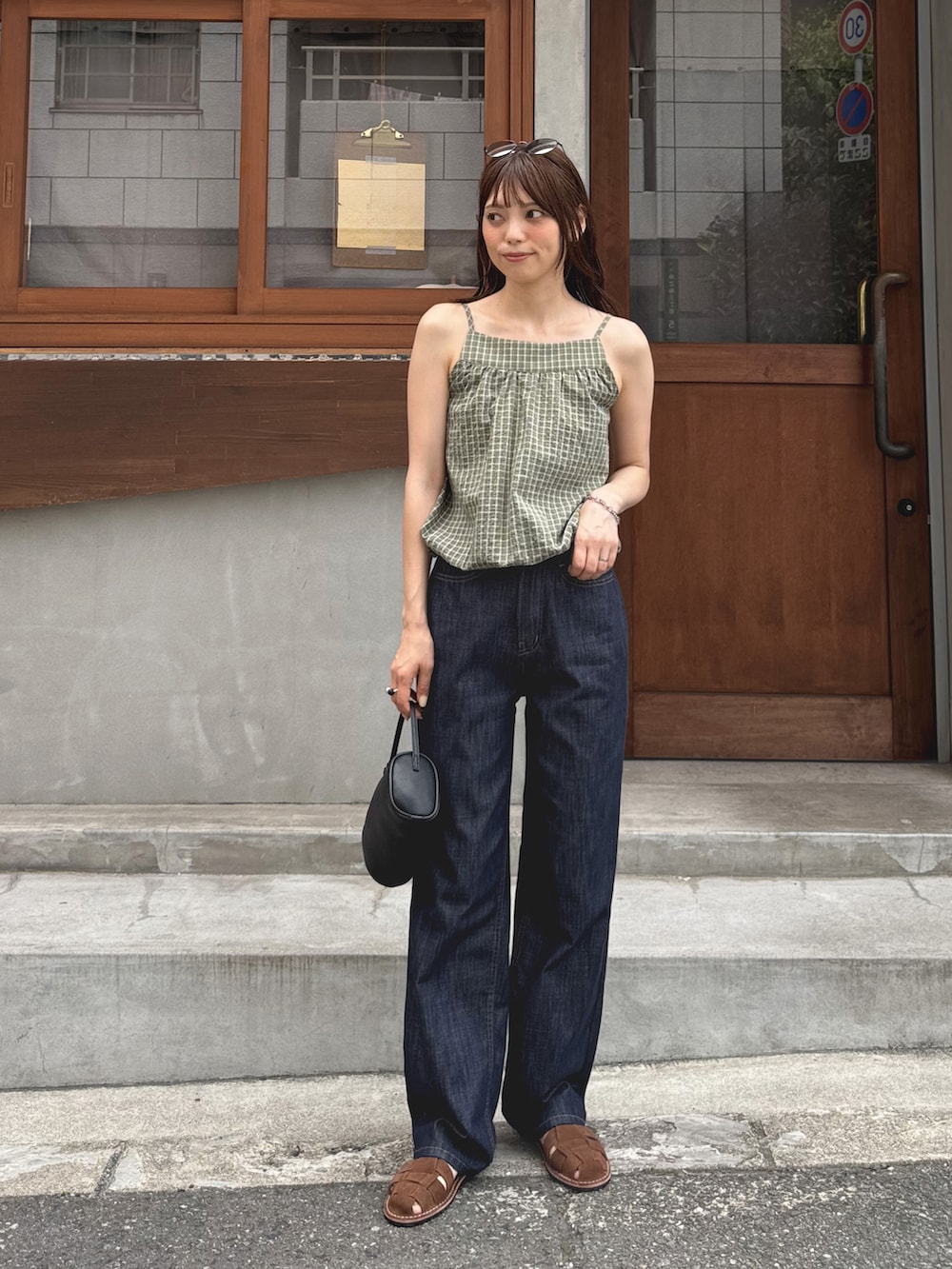 グリーン系のタンクトップ、ブルー系のデニムパンツ、ブラック系のショルダーバッグを着用したレディースの夏コーディネートの3枚目の写真