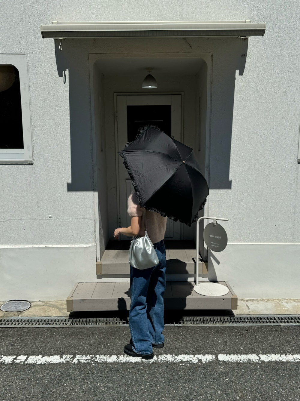 ブルー系のデニムパンツ、シルバー系のショルダーバッグ、ブラック系の折りたたみ傘を着用したレディースの夏コーディネートの2枚目の写真