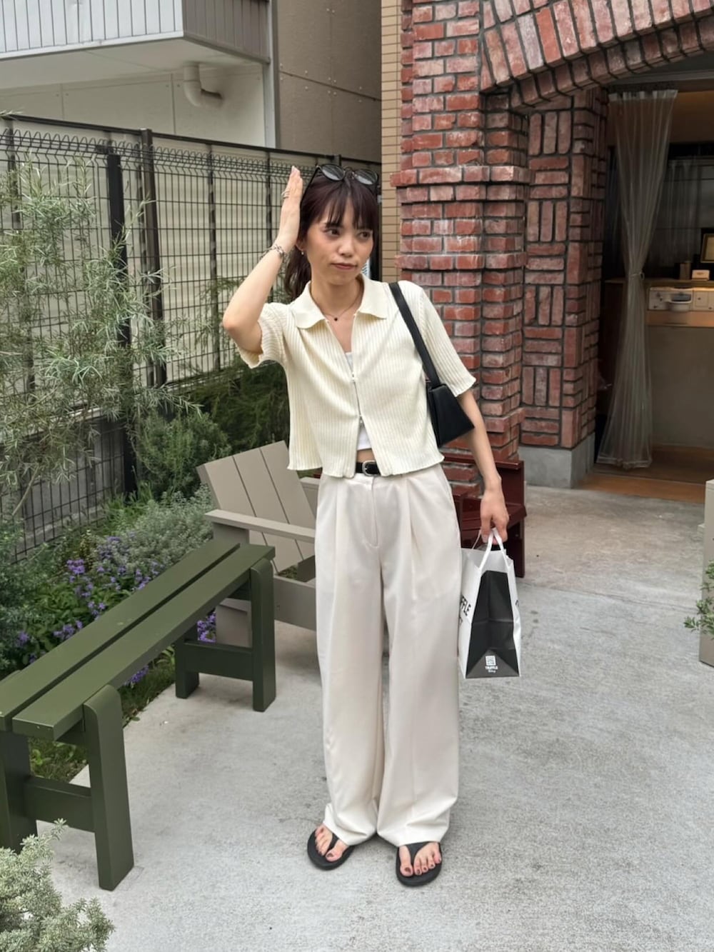 ホワイト系のニット/セーター、ホワイト系のスラックス、ブラック系のショルダーバッグを着用したレディースの夏コーディネートの4枚目の写真