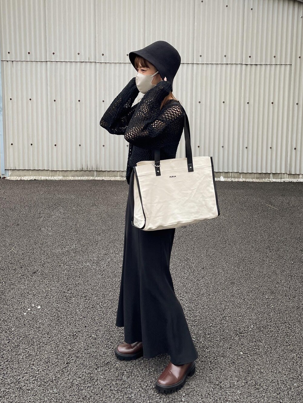 ブラック系のニット/セーター、ホワイト系のトートバッグ、ブラウン系のブーツを着用したレディースの秋コーディネートの2枚目の写真