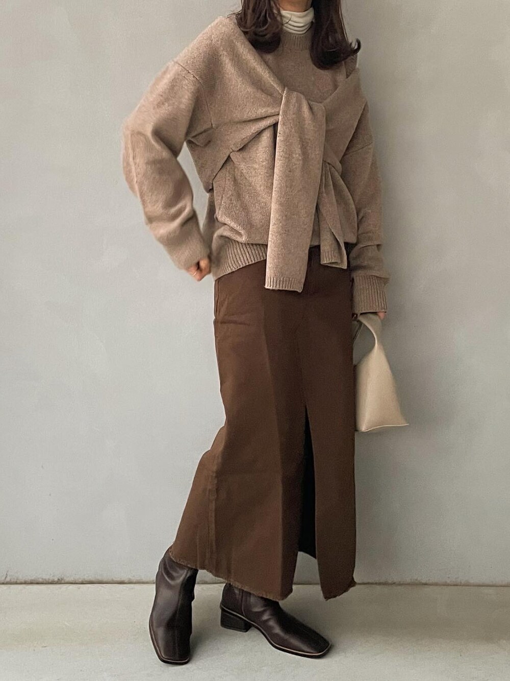 ベージュ系のニット/セーター、ホワイト系のハンドバッグ、ブラウン系のブーツを着用したレディースの冬コーディネートの2枚目の写真