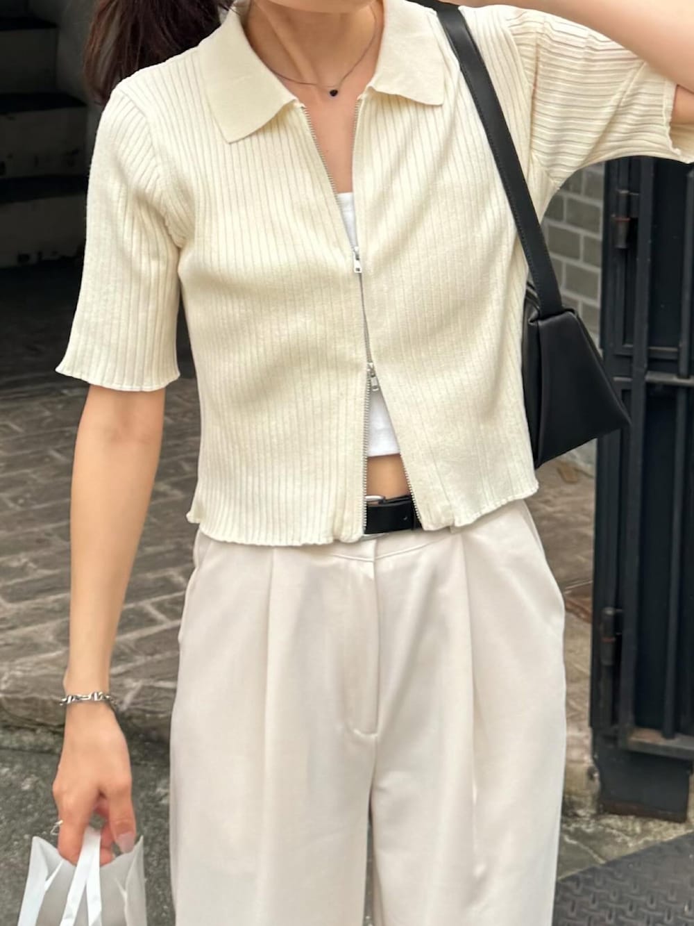 ホワイト系のニット/セーター、ホワイト系のスラックス、ブラック系のショルダーバッグを着用したレディースの夏コーディネートの2枚目の写真