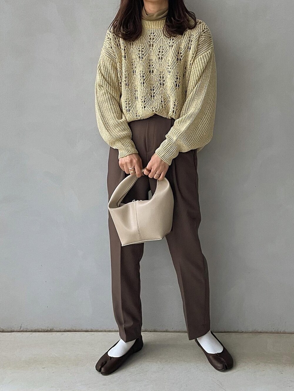 グリーン系のニット/セーター、ホワイト系のハンドバッグを着用したレディースの冬コーディネートの2枚目の写真