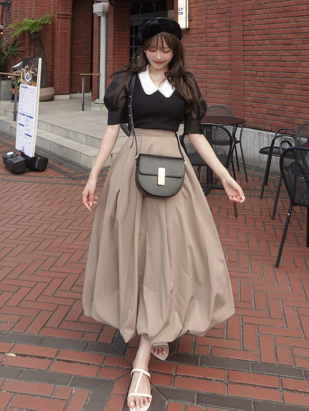 ベージュ系のスカート、ホワイト系のサンダル、ブラック系のニット/セーターを着用したレディースの夏コーディネートの2枚目の写真