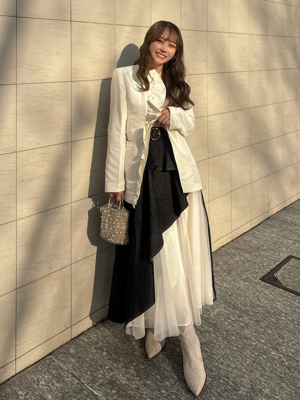ベージュ系のブーツ、ゴールド系のバッグ、ホワイト系のトップスを着用したレディースの春コーディネートの2枚目の写真