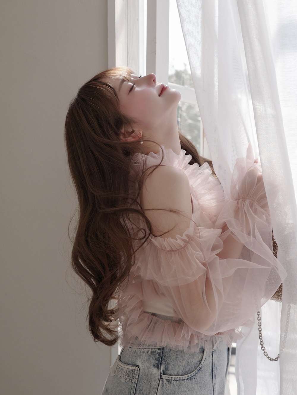 ピンク系のトップス、ゴールド系のバッグ、ブルー系のパンツを着用したレディースの春コーディネートの3枚目の写真