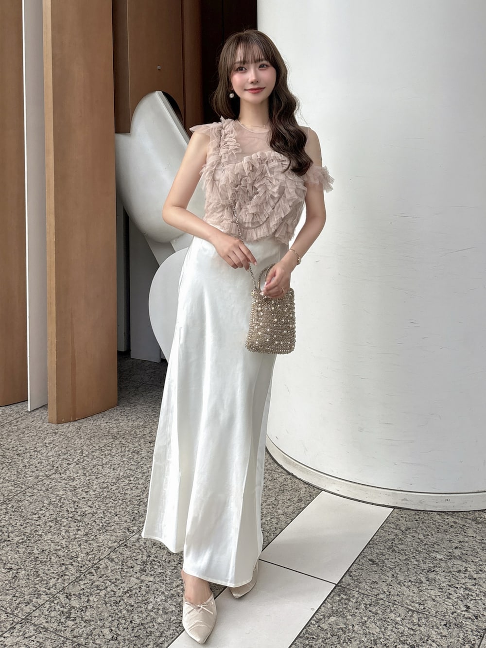 ホワイト系のスカート、ピンク系のトップス、ゴールド系のバッグを着用したレディースの夏コーディネートの2枚目の写真