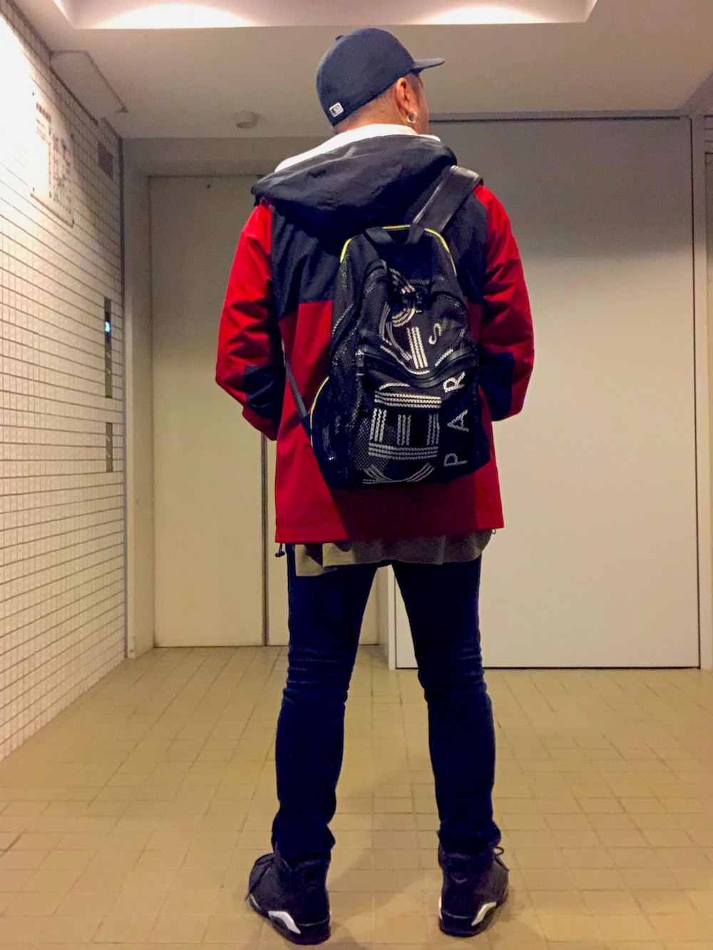 レッド系のブルゾン、ブルー系のデニムパンツ、ブラック系のスニーカーを着用したメンズの秋コーディネートの4枚目の写真