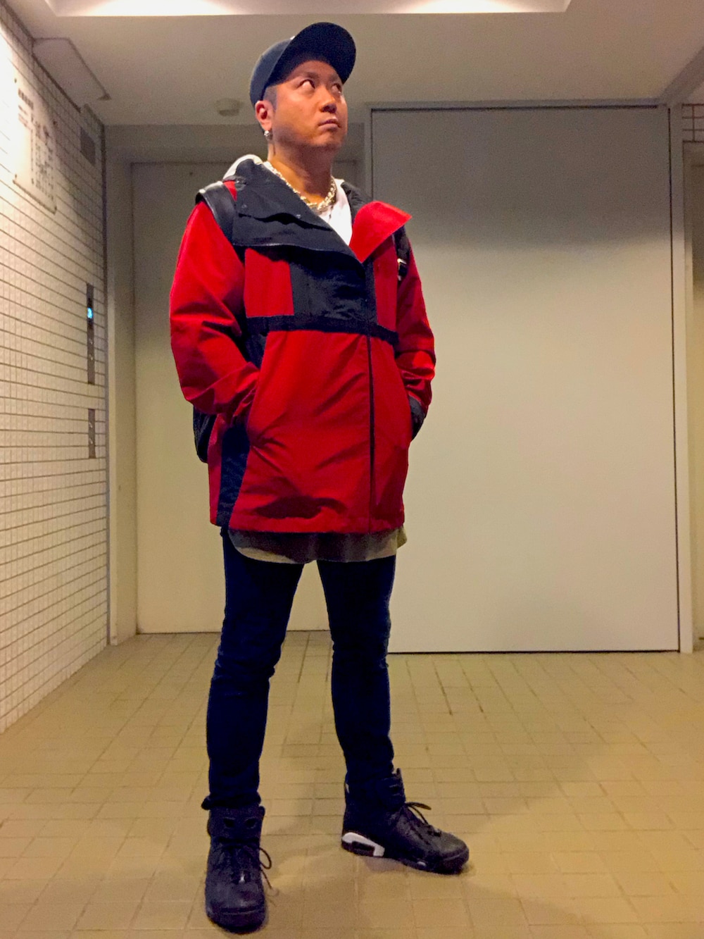 レッド系のブルゾン、ブルー系のデニムパンツ、ブラック系のスニーカーを着用したメンズの秋コーディネートの2枚目の写真