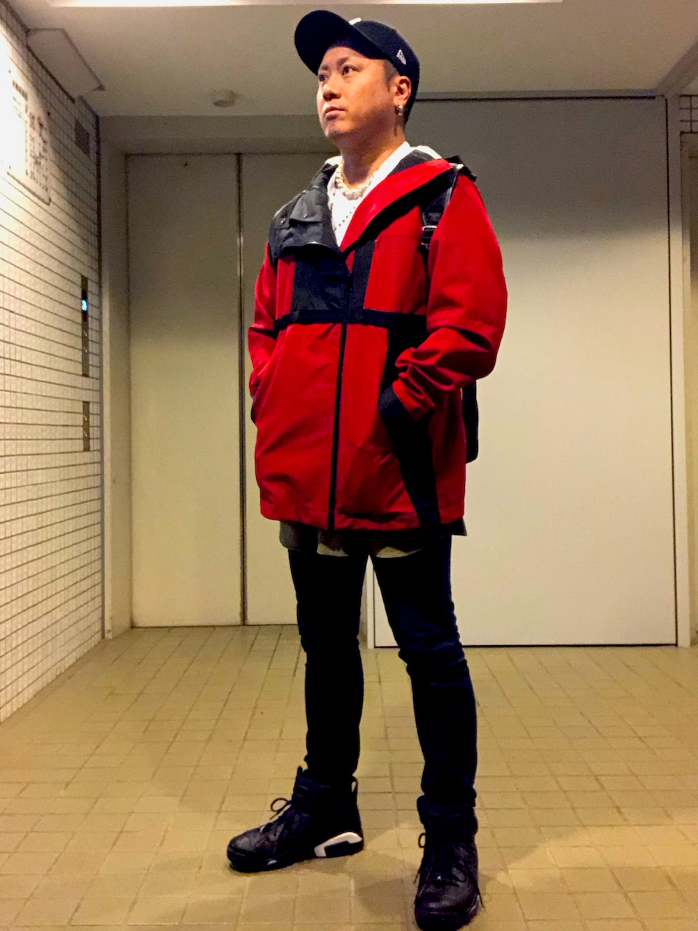 レッド系のブルゾン、ブルー系のデニムパンツ、ブラック系のスニーカーを着用したメンズの秋コーディネートの3枚目の写真