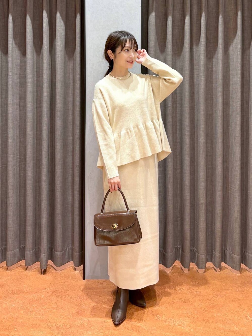 ブラウン系のボストンバッグ、ブラウン系のブーツ、ホワイト系のワンピースを着用したレディースの秋コーディネートの3枚目の写真