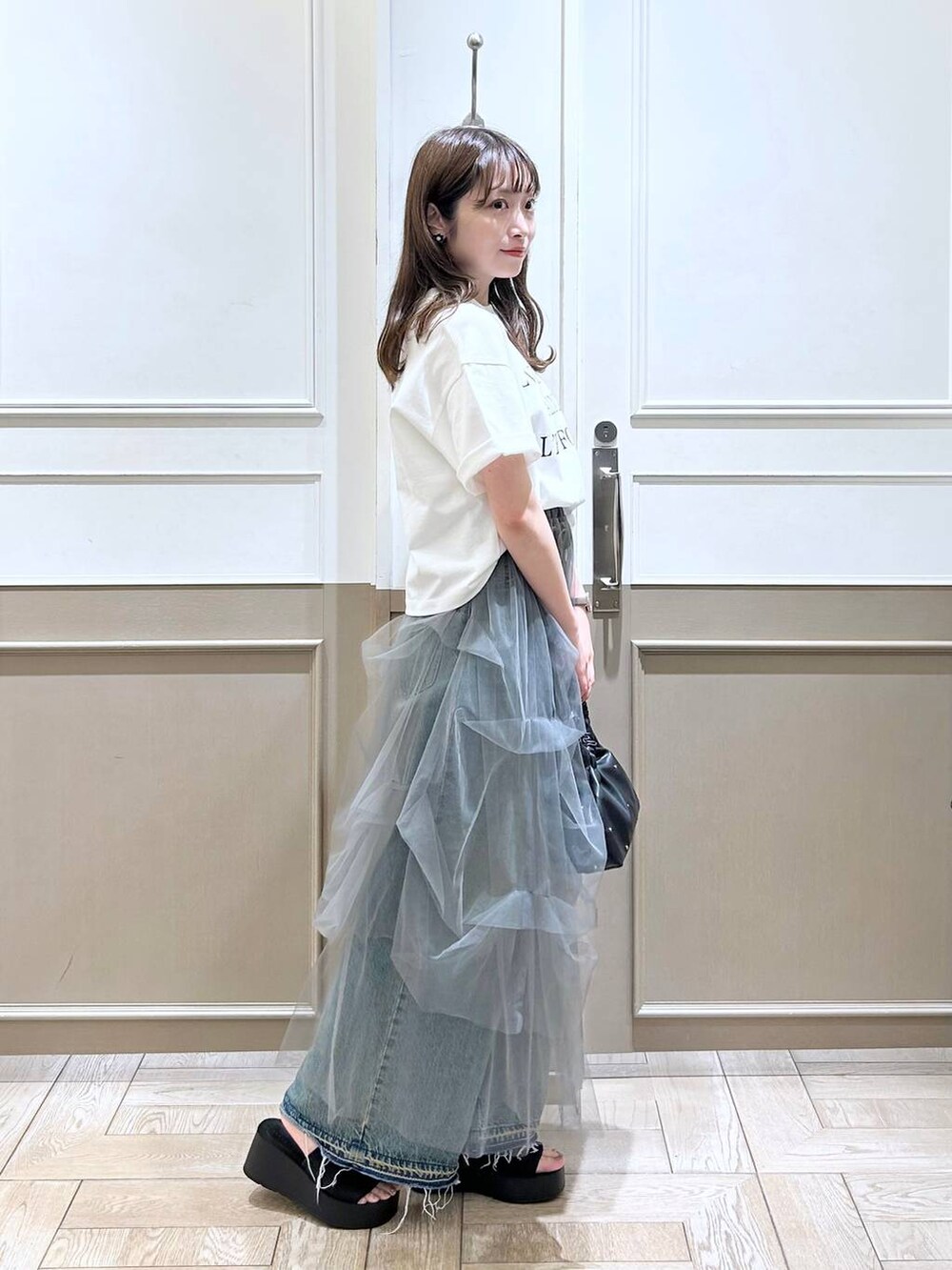 ブラック系のハンドバッグ、ブラック系のサンダル、ブルー系のデニムパンツを着用したレディースの夏コーディネートの3枚目の写真