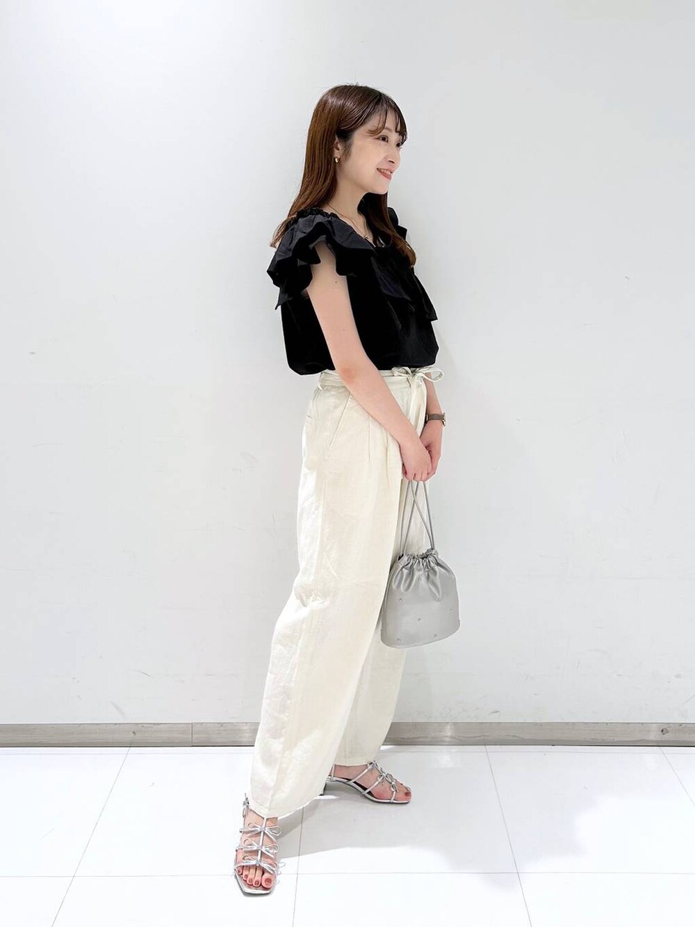 シルバー系のショルダーバッグ、シルバー系のサンダル、ホワイト系のスラックスを着用したレディースの夏コーディネートの3枚目の写真