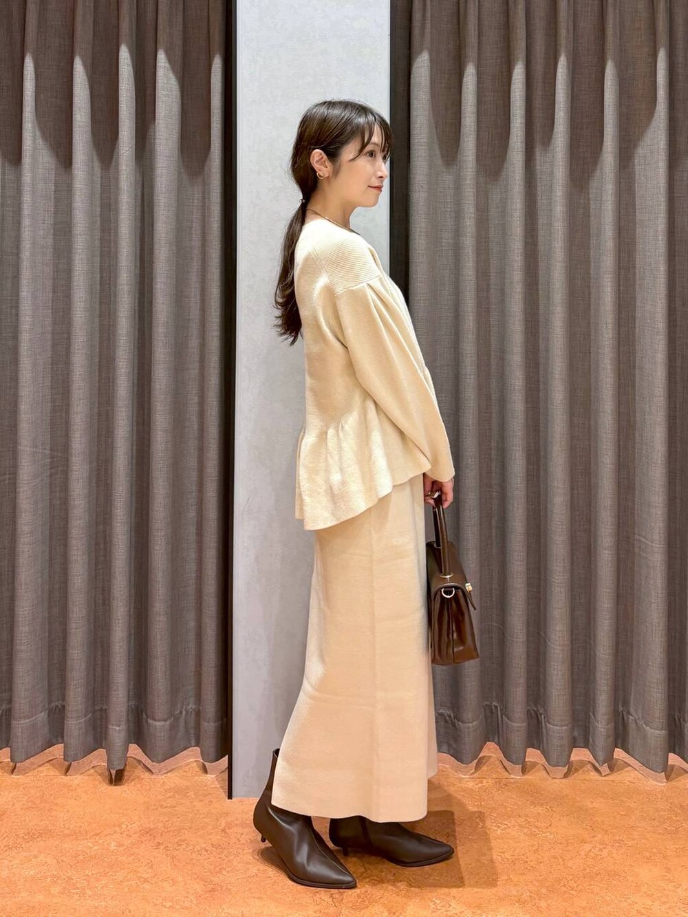 ブラウン系のボストンバッグ、ブラウン系のブーツ、ホワイト系のワンピースを着用したレディースの秋コーディネートの5枚目の写真