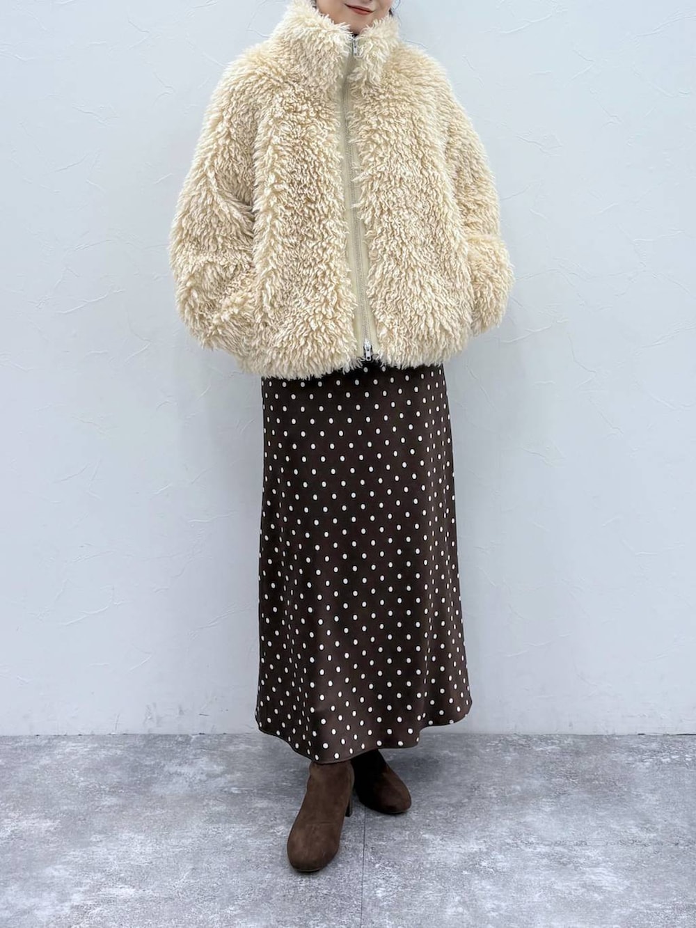 ブラウン系のスカート、ブラウン系のブーツ、ホワイト系のブルゾンを着用したレディースの秋コーディネートの2枚目の写真