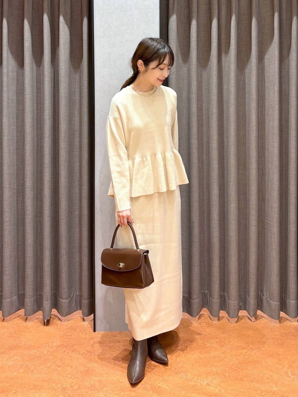 ブラウン系のボストンバッグ、ブラウン系のブーツ、ホワイト系のワンピースを着用したレディースの秋コーディネートの2枚目の写真