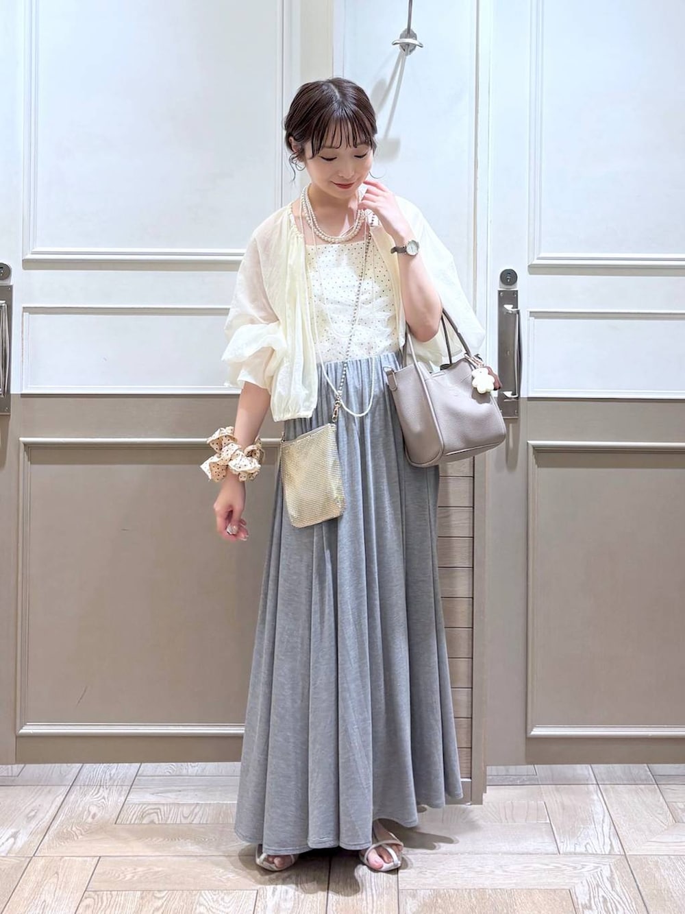 ゴールド系のショルダーバッグ、ホワイト系のサンダル、ホワイト系のブルゾンを着用したレディースの夏コーディネートの2枚目の写真