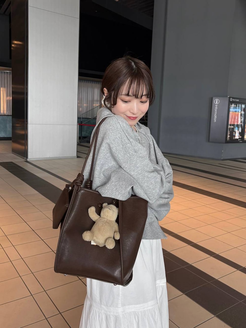 グレー系のパーカー、ブラウン系のトートバッグ、ホワイト系のパンプスを着用したレディースの春コーディネートの7枚目の写真