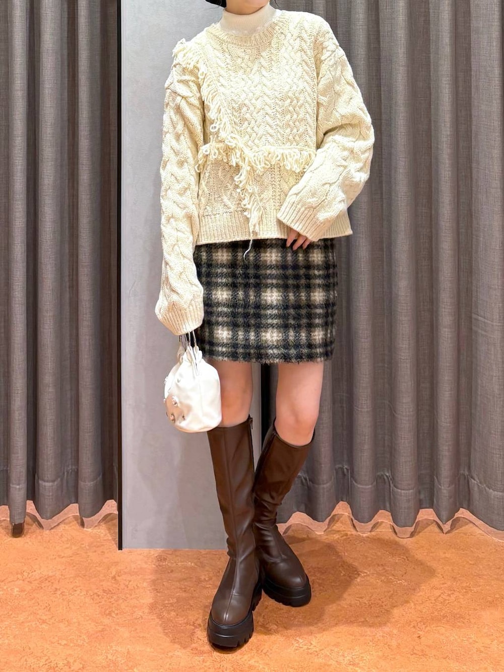 ブラウン系のステンカラーコート、ホワイト系のニット/セーター、ブラウン系のブーツを着用したレディースの冬コーディネートの6枚目の写真