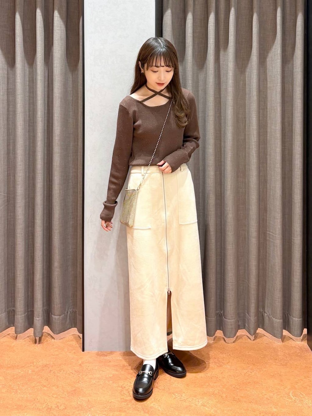 ゴールド系のショルダーバッグ、ホワイト系のスカート、ブラック系のローファーを着用したレディースの秋コーディネートの2枚目の写真