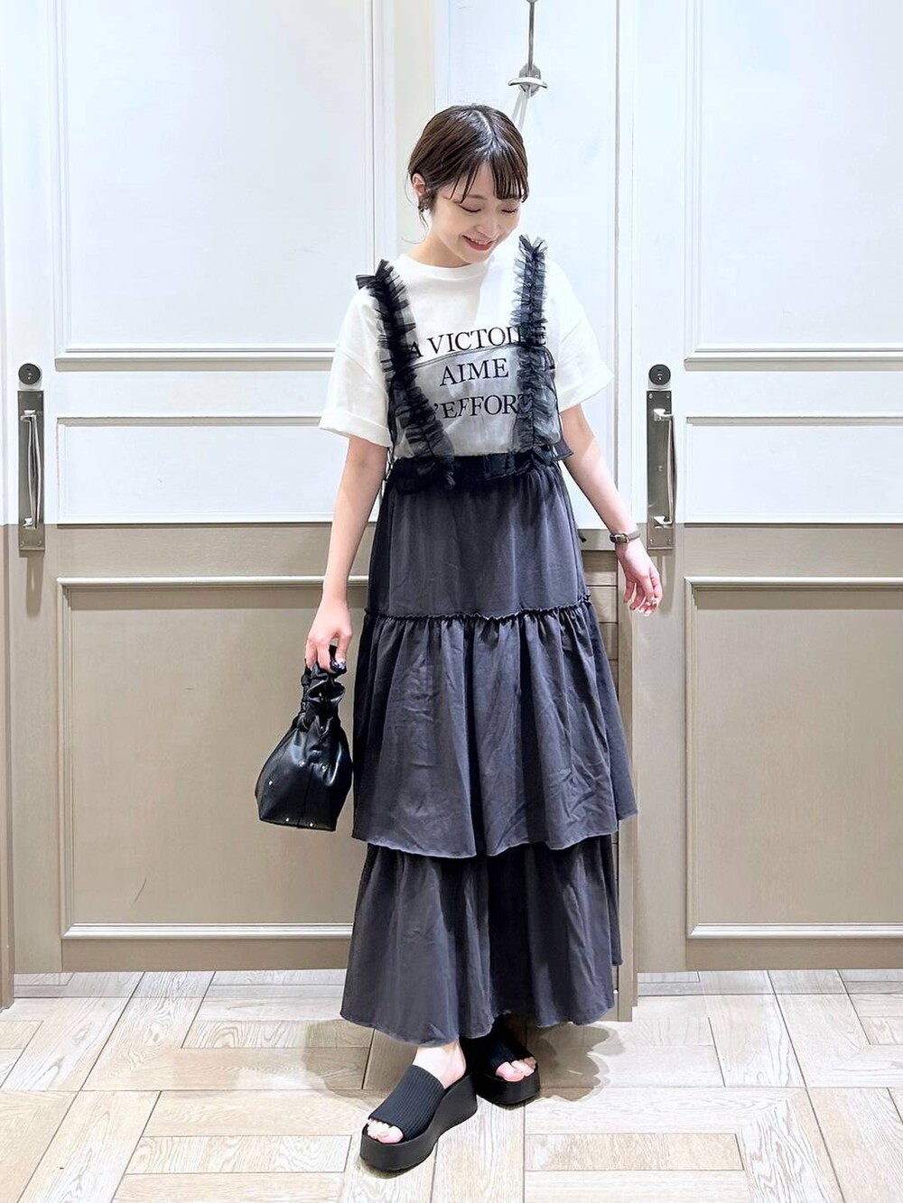 ブラック系のハンドバッグ、ブラック系のサンダル、ブラック系のベストを着用したレディースの夏コーディネートの2枚目の写真