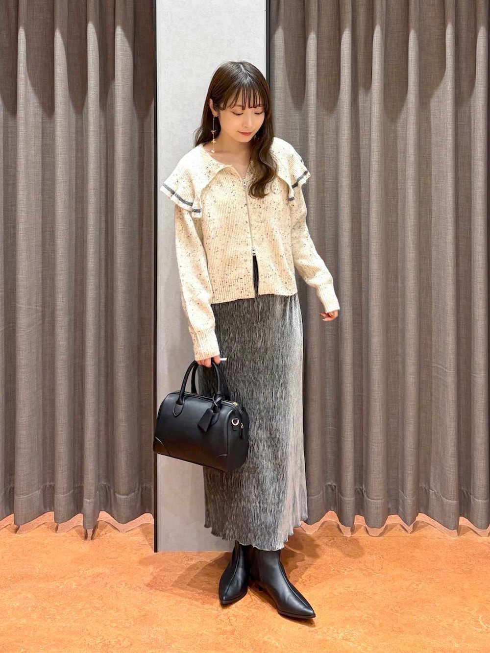 ブラック系のショルダーバッグ、ベージュ系のニット/セーター、グレー系のスカートを着用したレディースの秋コーディネートの2枚目の写真