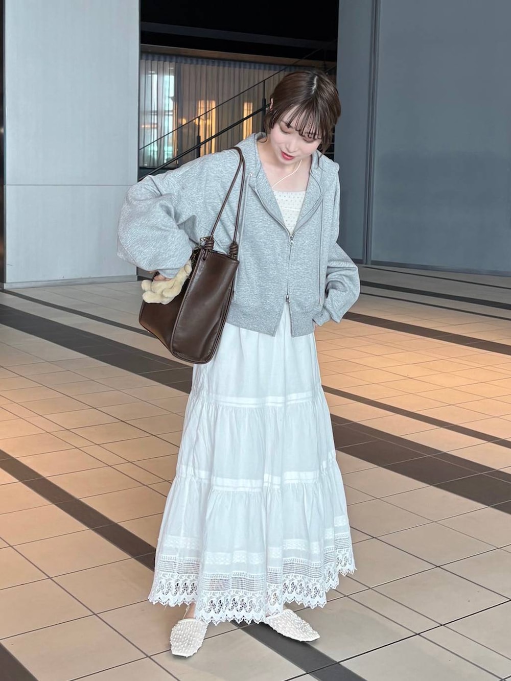 グレー系のパーカー、ブラウン系のトートバッグ、ホワイト系のパンプスを着用したレディースの春コーディネートの2枚目の写真