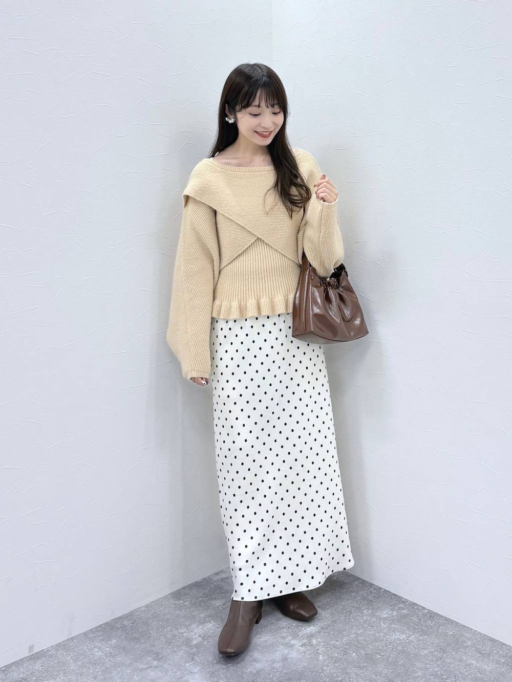 ホワイト系のスカート、ベージュ系のニット/セーター、ブラウン系のブーツを着用したレディースの秋コーディネートの2枚目の写真