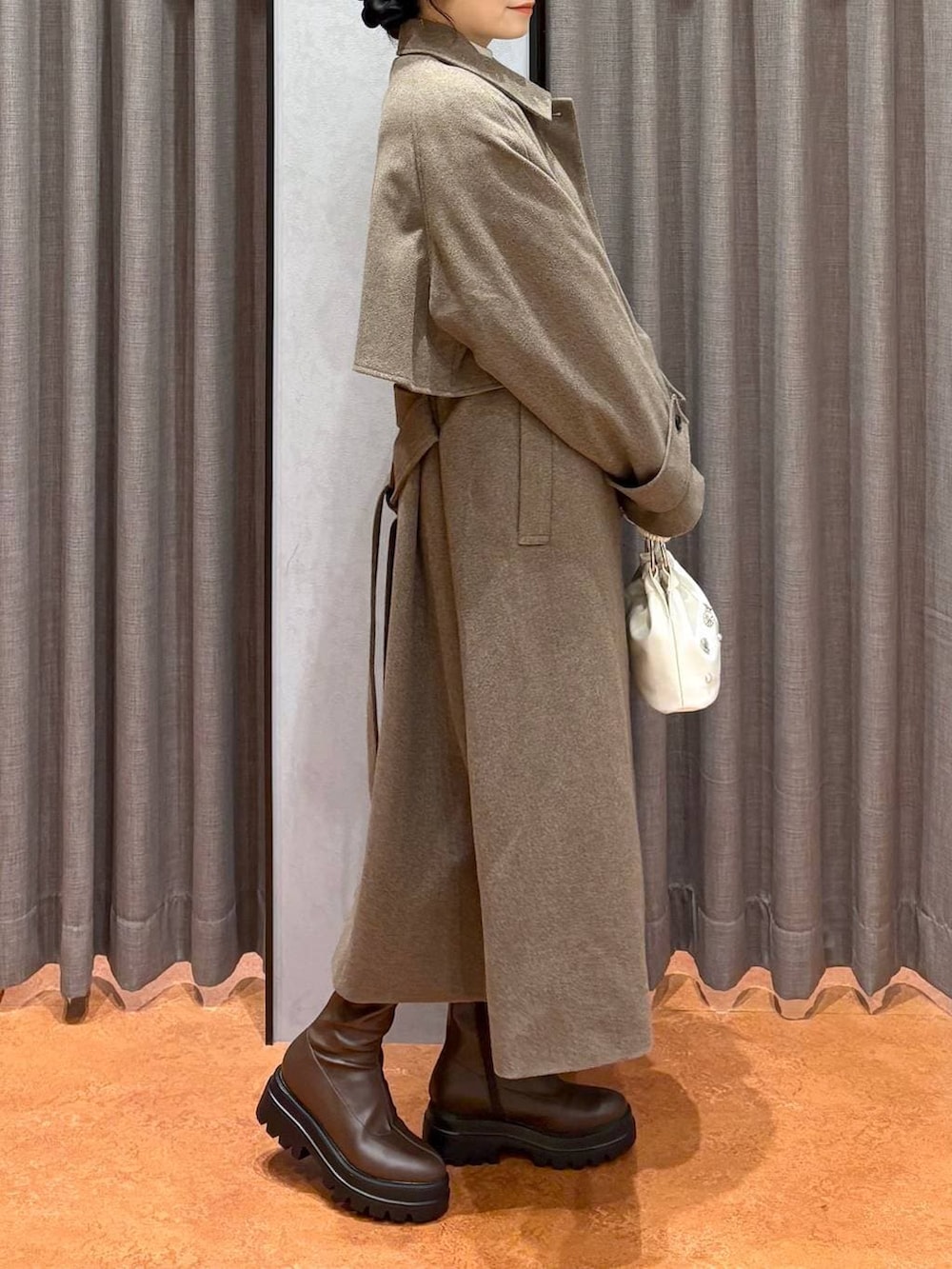 ブラウン系のステンカラーコート、ホワイト系のニット/セーター、ブラウン系のブーツを着用したレディースの冬コーディネートの3枚目の写真