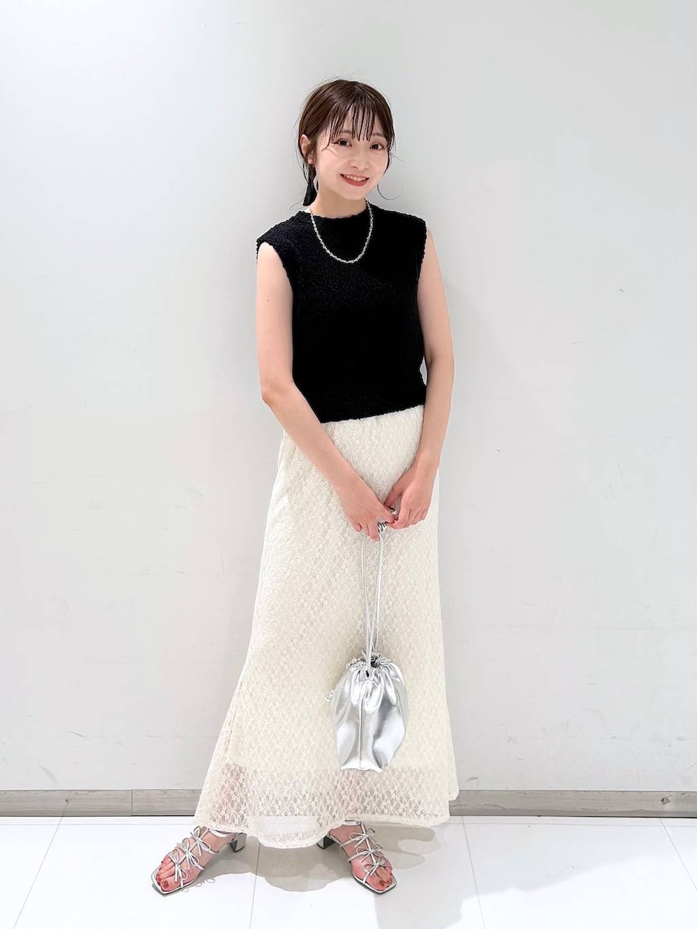 シルバー系のサンダル、ホワイト系のスカート、ブラック系のベストを着用したレディースの夏コーディネートの2枚目の写真