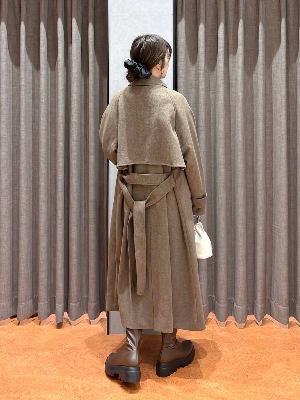 ブラウン系のステンカラーコート、ホワイト系のニット/セーター、ブラウン系のブーツを着用したレディースの冬コーディネートの4枚目の写真