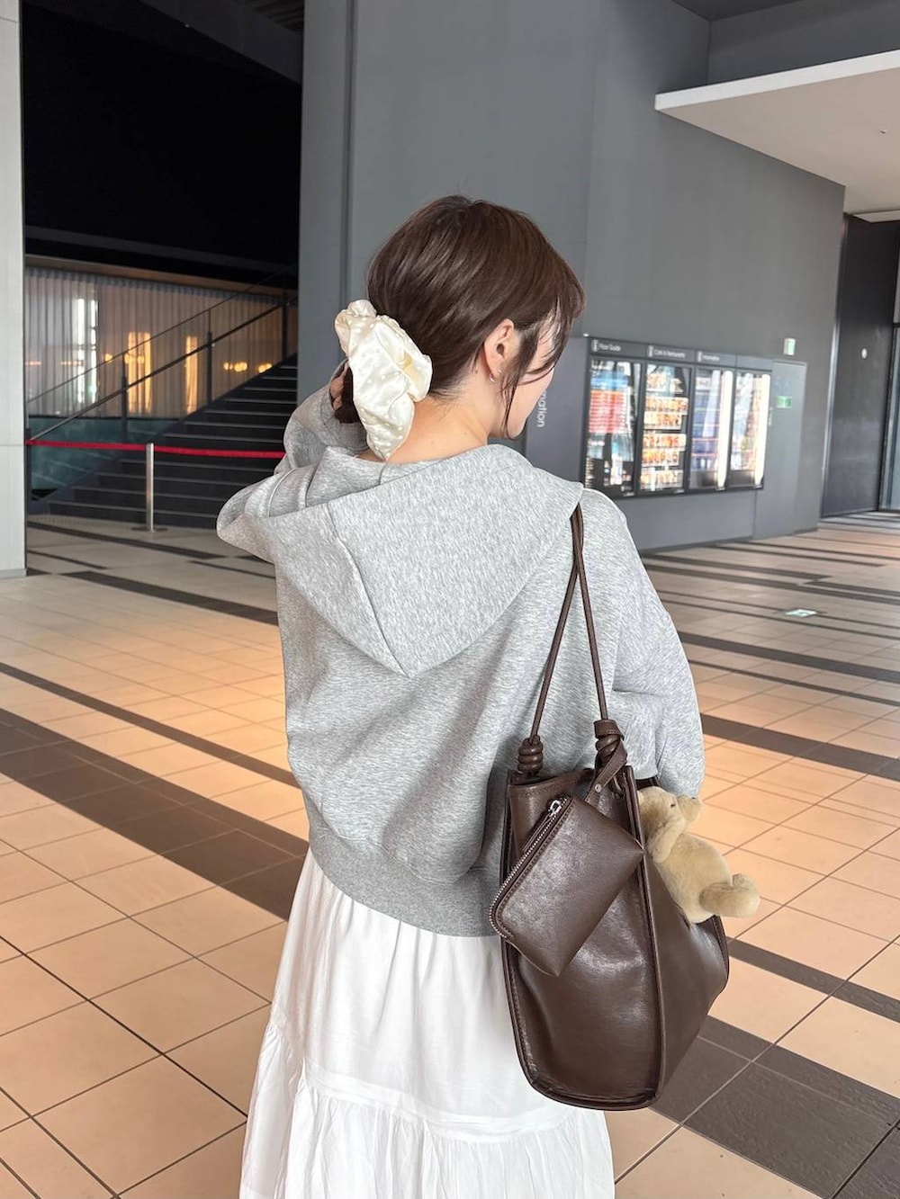 グレー系のパーカー、ブラウン系のトートバッグ、ホワイト系のパンプスを着用したレディースの春コーディネートの5枚目の写真