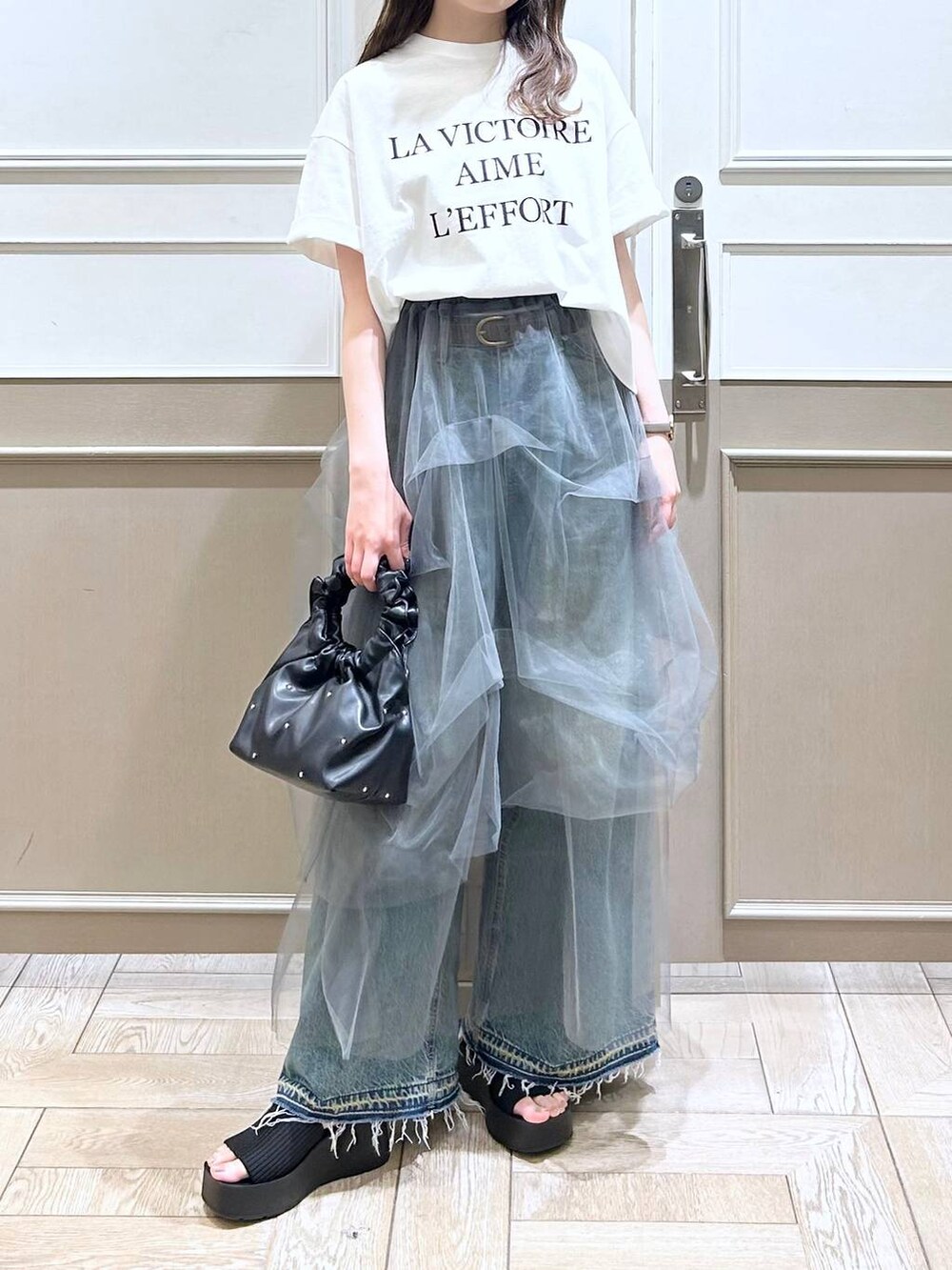 ブラック系のハンドバッグ、ブラック系のサンダル、ブルー系のデニムパンツを着用したレディースの夏コーディネートの2枚目の写真