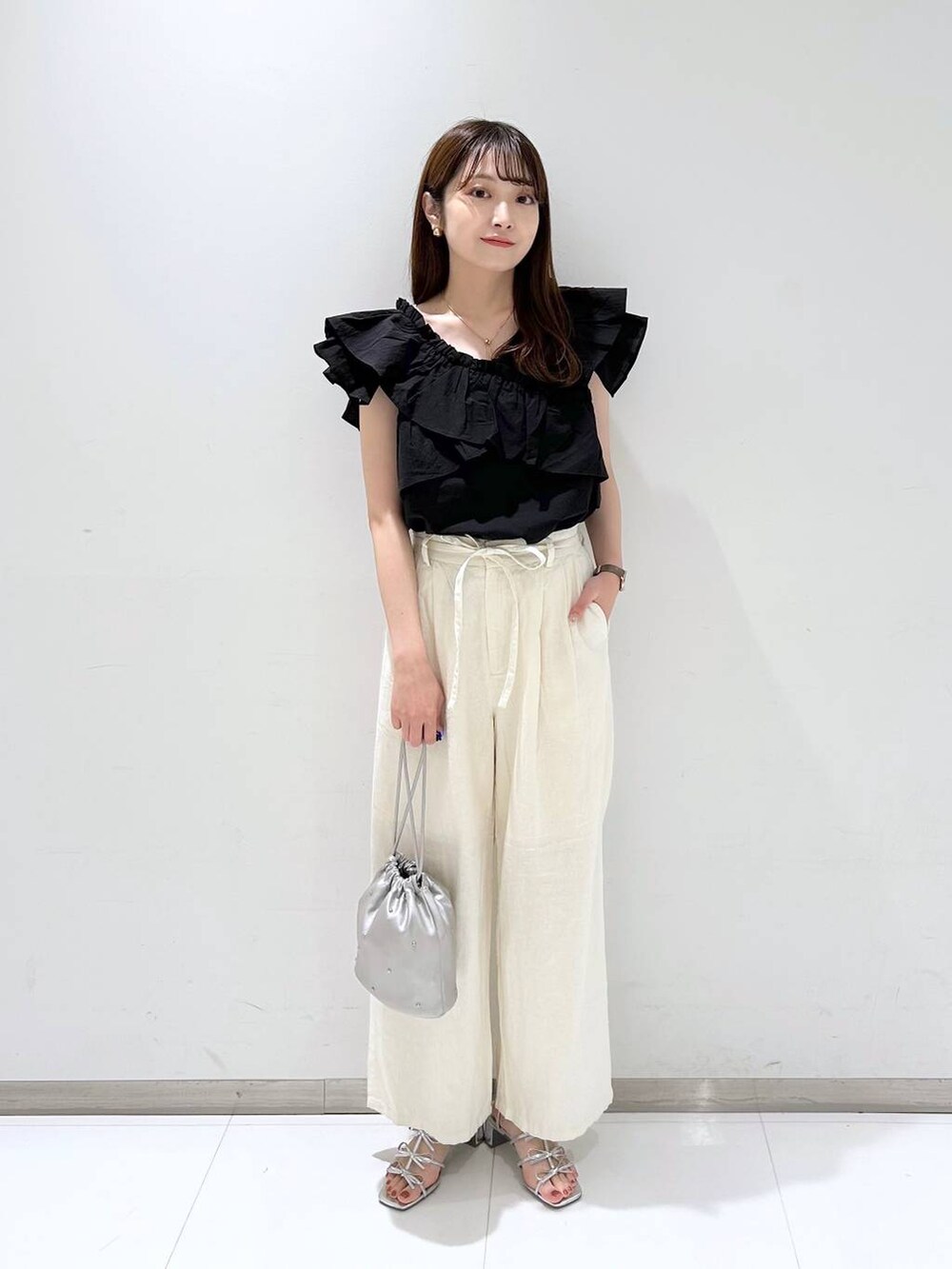 シルバー系のショルダーバッグ、シルバー系のサンダル、ホワイト系のスラックスを着用したレディースの夏コーディネートの2枚目の写真