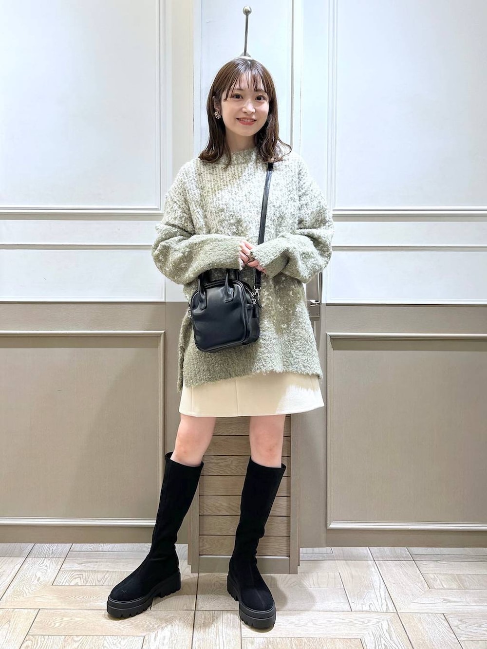 ブラック系のブーツ、ホワイト系のスカート、グリーン系のニット/セーターを着用したレディースの秋コーディネートの2枚目の写真