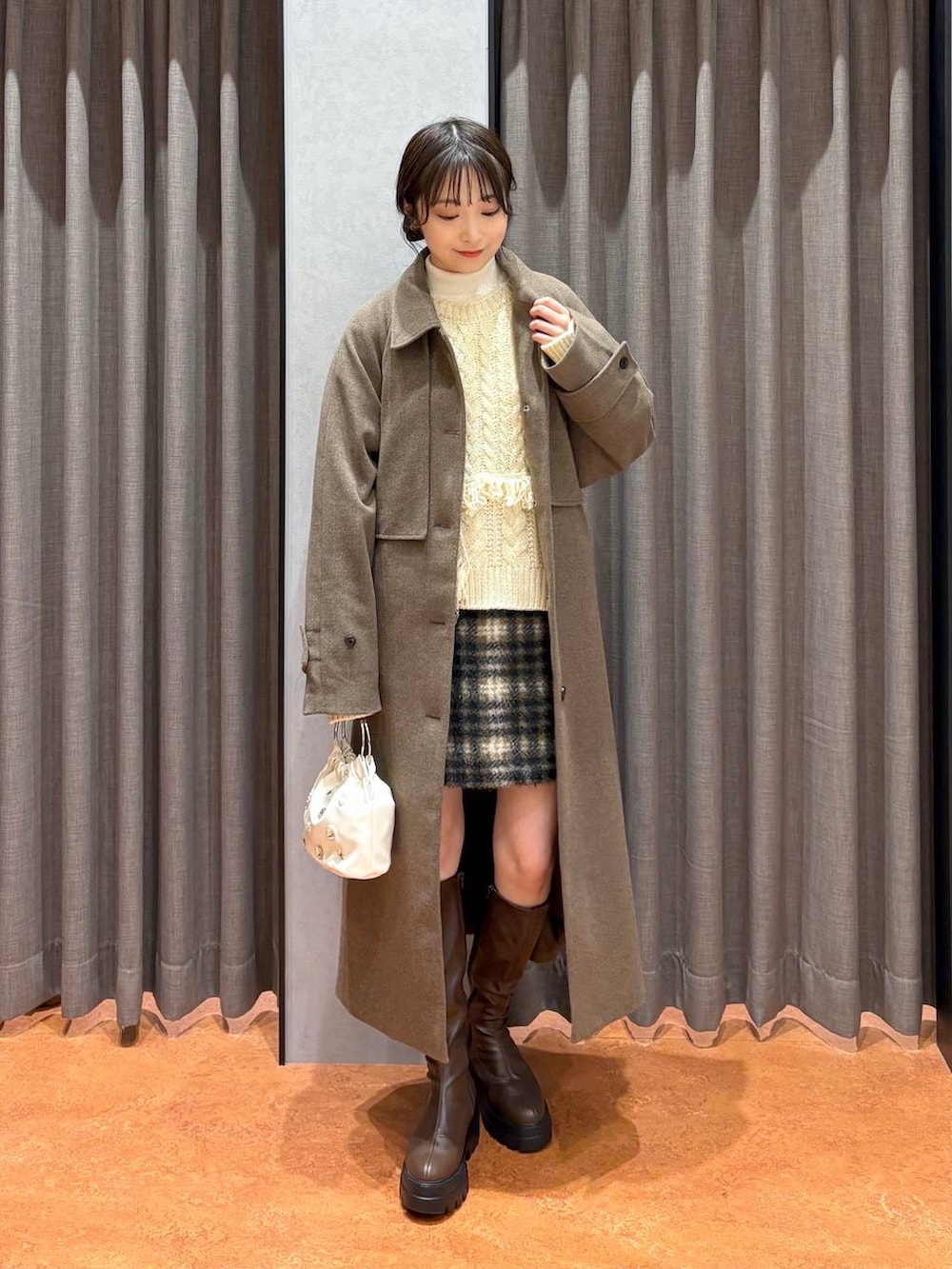 ブラウン系のステンカラーコート、ホワイト系のニット/セーター、ブラウン系のブーツを着用したレディースの冬コーディネートの2枚目の写真