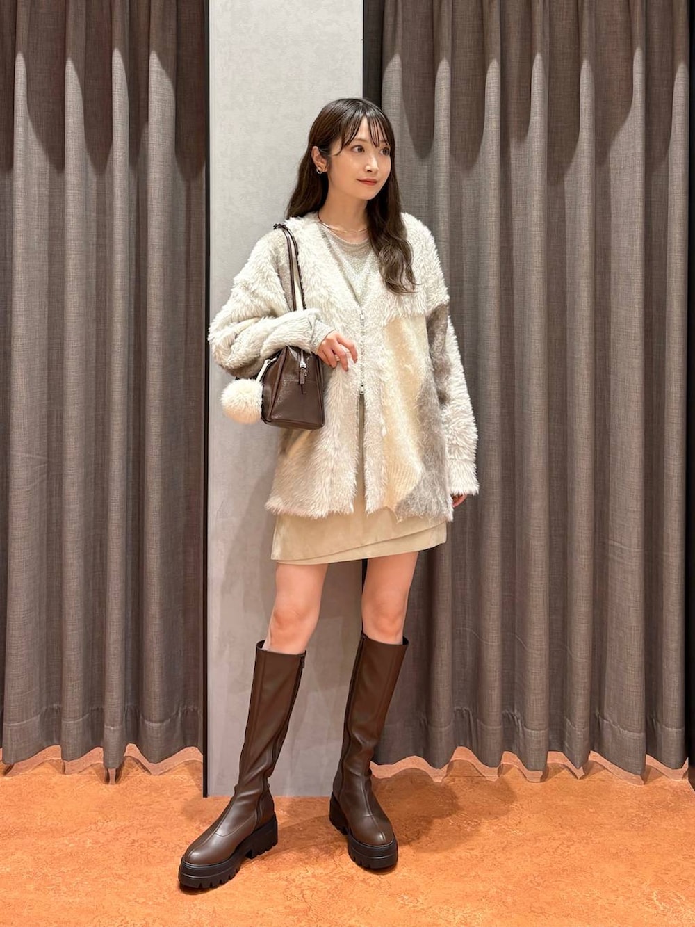 ホワイト系のカーディガン/ボレロ、ホワイト系のスカート、ブラウン系のブーツを着用したレディースの秋コーディネートの2枚目の写真