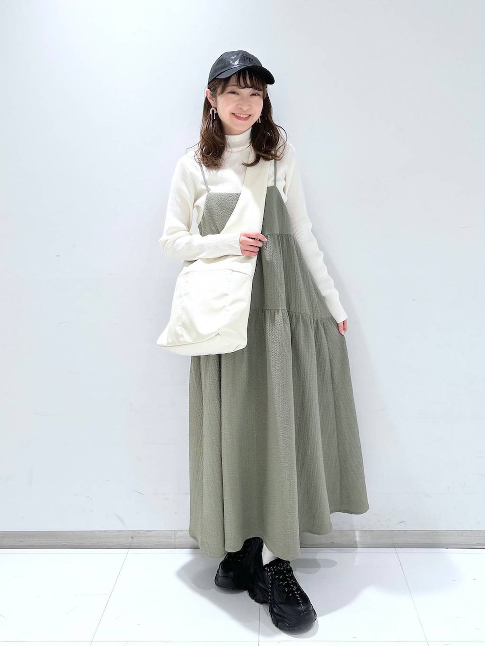 グリーン系のワンピース、ホワイト系のニット/セーター、ブラック系のスニーカーを着用したレディースの冬コーディネートの2枚目の写真