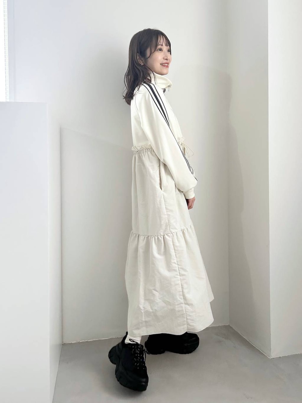 ブラック系のスニーカー、ホワイト系のワンピース、ゴールド系のイヤリングを着用したレディースの冬コーディネートの2枚目の写真